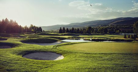 Sicht auf Fairway und Green einer Golfanlage, Berge im Hintergrund.